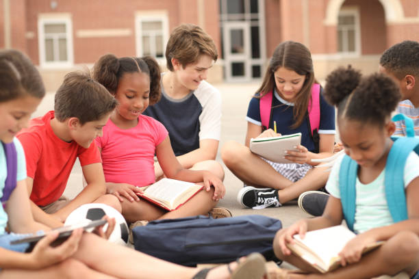 Mixed age, multi-ethnic group of elementary and junior high age student friends talk, study together outside the school building. Caucasian, latin, and african descent.